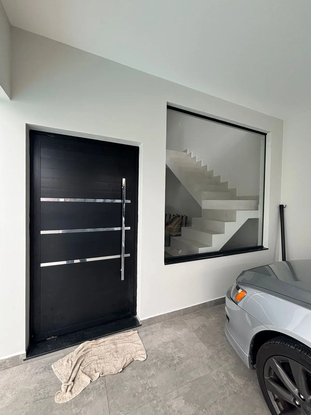 Hall de entrada com porta pivotante de alumínio preto e painel de vidro fixo com vista para a escada