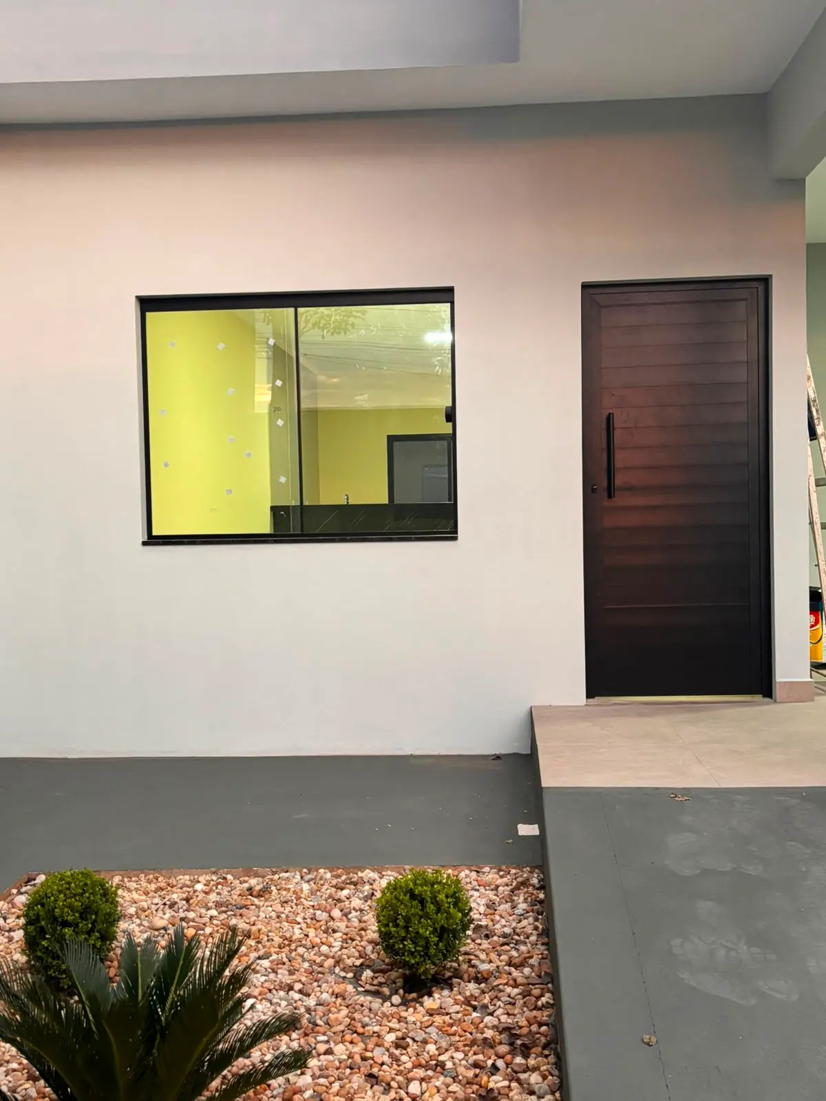 Fachada com janela de alumínio preto e porta pivotante de madeira